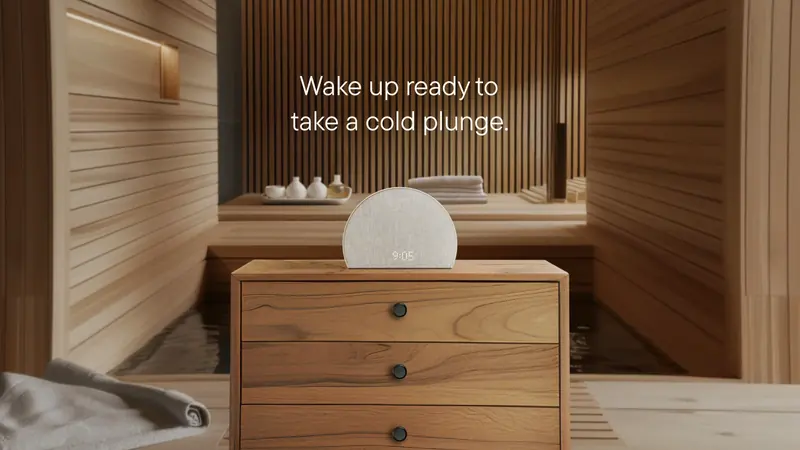 Le même réveil sur une table de chevet dans un sauna en bois, avec l’accroche en anglais « Wake up ready to take a cold plunge » (se réveiller prêt pour un bain froid).